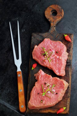 Siyah arka plan çiğ taze mermer et Steak fileto mignon ve rustik kesme tahtası maydanoz ve kırmızı biber ile et çatalı