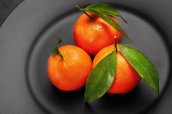 Tangerinas laranja maduras com folhas verdes em placa preta e mate. Conceito de nutrição saudável, dieta, desintoxicação. Foco seletivo.Fechar — Fotografia de Stock