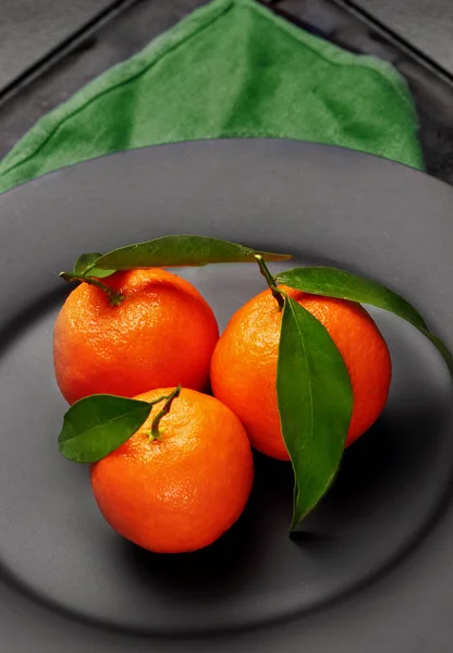 Dojrzały pomarańczowy mandarynki z zielonych liści na czarne, matowe płytki. Pojęcie zdrowego odżywiania, diety detox. Selektywny fokus. Zbliżenie — Zdjęcie stockowe
