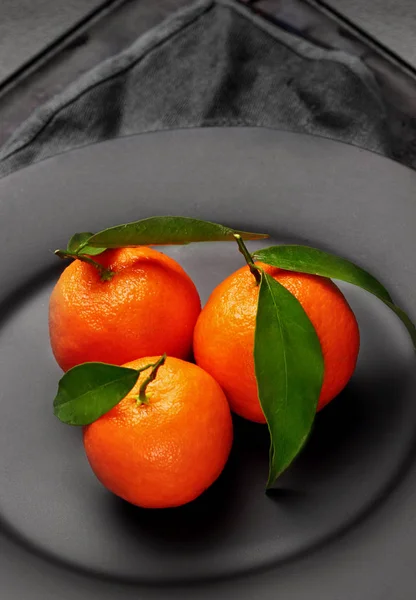 Mandarinas anaranjadas maduras con hojas verdes sobre plato negro mate. Concepto de nutrición saludable, dieta, desintoxicación. Enfoque selectivo.Primer plano —  Fotos de Stock