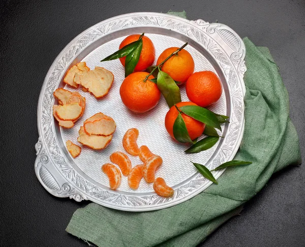 Still life.Fresh tangerina clementina com folhas em bandeja de prata no fundo de pedra escura, vista superior — Fotografia de Stock