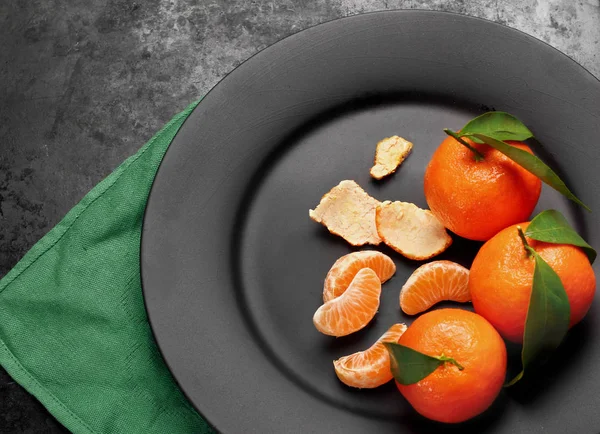 Спелые оранжевые мандарины с зелеными листьями на черной матовой пластине  , — стоковое фото