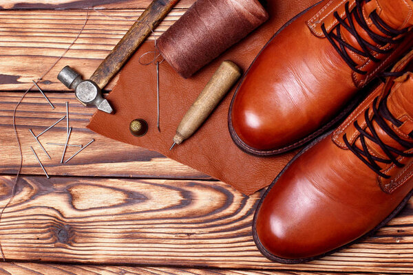 Leather boots and bootmaker tools awl, nails, skien of thread .Wooden background.Concept tools bootmaker.top view. copy space