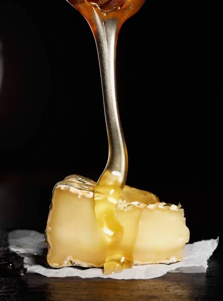 Stukje camembert met met honing gieten van honing lepel. Zwarte achtergrond — Stockfoto
