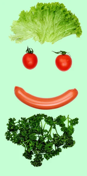 Happy smilingface from food- sausage mouth, hair - salad, eyes tomatoes, beard parsley.Concept funny food.Food art.Food emotion.green background — Stock Photo, Image