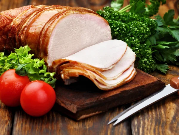 Delicious smoked ham sliced on a wooden rustic board with tomatoes cherry, parsley and leaf of salad, knife.wooden background.Closeup selective focus — Stock Photo, Image