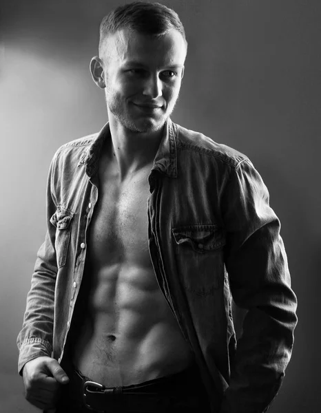Handsome young man with perfect muscule body dressed in denim shirt and jeans posing.Black and white photo — Stock Photo, Image