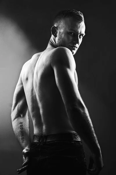 Back of andsome young man with perfect muscule body dressed in jeans standing bakc to us and see agressive.Black and white photo — Stock Photo, Image