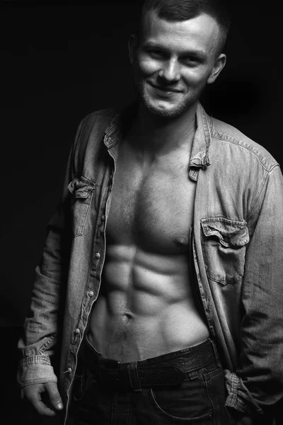 Handsome young man with perfect muscule body dressed in denim shirt and jeans posing.Black and white photo — Stock Photo, Image