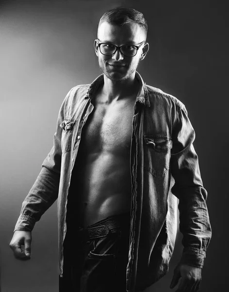 Fashion handsome young man with perfect muscule body dressed in denim shirt and jeans and stylish eyeglassesposing.Black and white photo — Stock Photo, Image