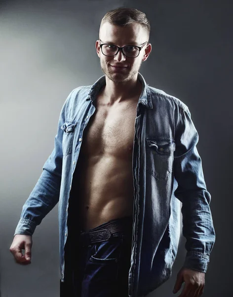 Fashion handsome young man with perfect muscule body dressed in denim shirt and jeans and stylish eyeglassesposing. — Stock Photo, Image