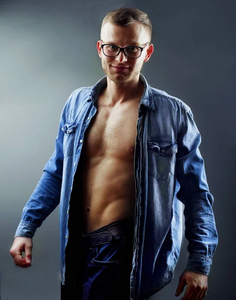 Fashion handsome young man with perfect muscule body dressed in denim shirt and jeans and stylish eyeglassesposing. — Stock Photo, Image