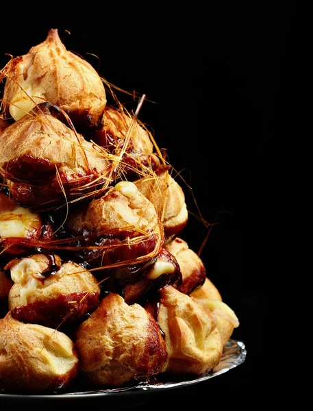 Pastel profiteroles con caramelo sobre fondo negro.Enfoque selectivo. Copiar espacio —  Fotos de Stock