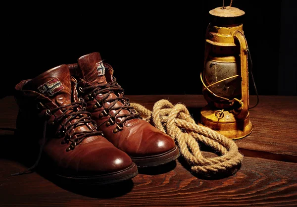 Натюрморт из дорожных ботинок, старая латерная керосиновая лампа и веревка на деревянном фоне — стоковое фото