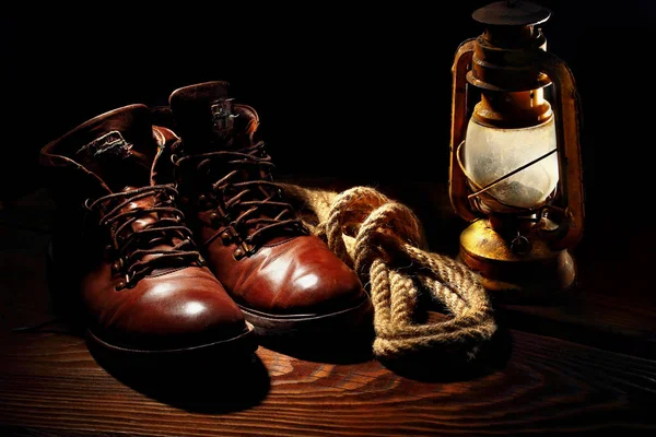 Натюрморт из дорожных ботинок, старая латерная керосиновая лампа и веревка на деревянном фоне — стоковое фото