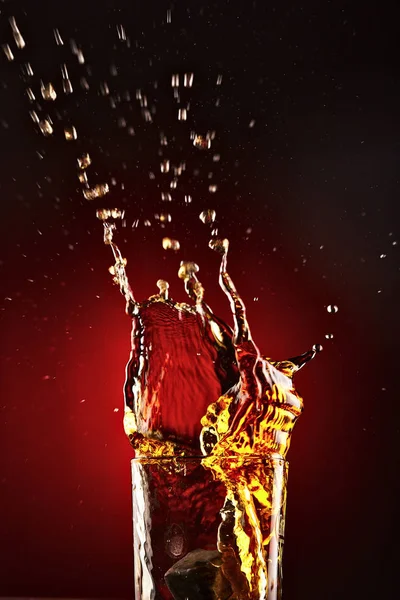 Zbliżenie: szkło z whisky splash. Na czerwonym tle. Koncepcja alkoholu splash — Zdjęcie stockowe