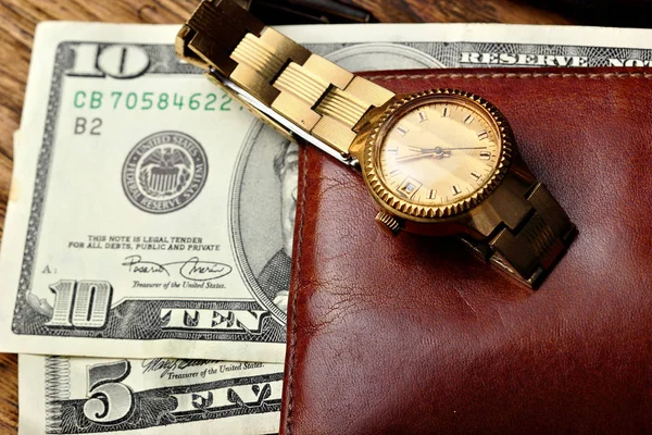 Елегантний золотий годинник і коричневий гаманець з грошима на дерев'яному столі — стокове фото