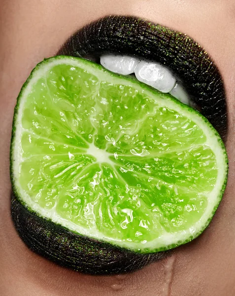 Primo piano di labbra di moda verde scuro che tengono la calce in bocca.Cosmetologia, farmacia o concetto di trucco di moda. Studio di bellezza girato. Primo piano — Foto Stock