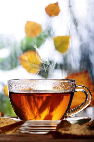 Taza de té en el alféizar de la ventana de madera con hojas de atumn amarillo.Ventana lluviosa desenfocada y árboles de otoño en plan srcond. —  Fotos de Stock