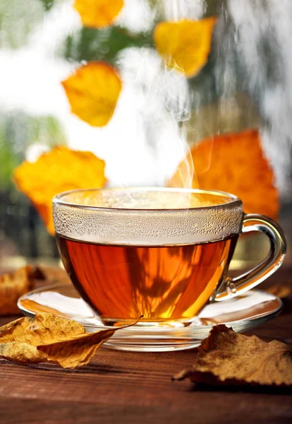 Taza de té en el alféizar de la ventana de madera con hojas de atumn amarillo.Ventana lluviosa desenfocada y árboles de otoño en plan srcond. —  Fotos de Stock