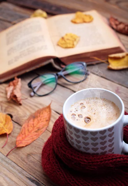 Copa de café capuchino caliente en la mesa de madera con hojas de otoño, libro y anteojos. Concepto de humor de otoño.. Imagen cálida de otoño. —  Fotos de Stock