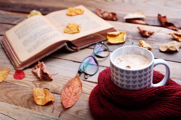 Copa de café capuchino caliente en la mesa de madera con hojas de otoño, libro y anteojos. Concepto de humor de otoño.. Imagen cálida de otoño. —  Fotos de Stock
