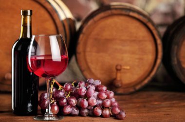 Kırmızı şarap. Cam ve şişe kırmızı şarap, üzüm ve varil ile natürmort. Seçici odak. Şarap mahzeni atmosfer. Kopya alanı