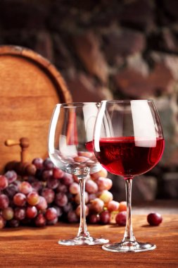 Kırmızı şarap. İki kadeh kırmızı şarap, üzüm ve namlu dolu ve boş ile natürmort. Seçici odak. Kopya alanı