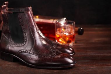 Chelsea boots kahverengi deri defocused cam ve şişe viski ile cilalı. Seçici odak. Çizmeler ağda. Uzay kopyalayın. Portre