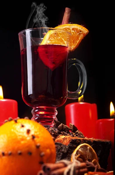 Glas av jul varm glögg på träbord med arter, apelsiner och röda ljus mot svart bakgrund. Closeup.Slective fokus — Stockfoto