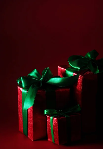 Κόκκινο δώρο κουτιά με πράσινα κορδόνια και φιόγκο στο φόντο σκούρο κόκκινο για διακοπές. Χαρούμενα Χριστούγεννα κάρτα. Θέμα "Χειμώνας Χριστούγεννα". Boxing day — Φωτογραφία Αρχείου