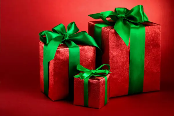 Röd presentförpackning med gröna band och rosett på röda holiday bakgrund. Merry christmas card. Vinter xmas tema. Annandag jul — Stockfoto