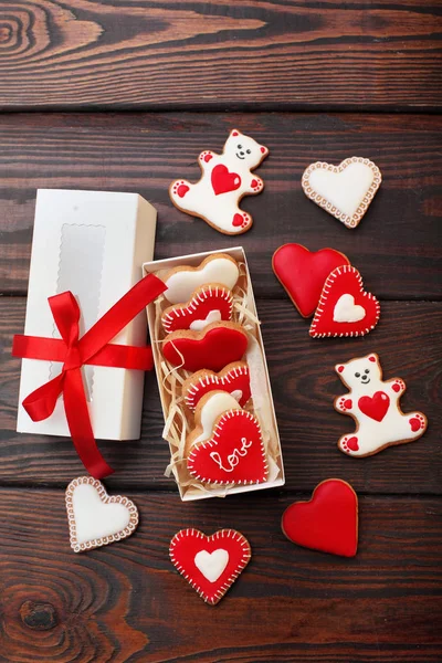 Red cookies hearts, white bears with red icing and white box with ribbon bow on the brown wooden table.Gift for Valentine 's Day .Valentine day background.Top view — стоковое фото