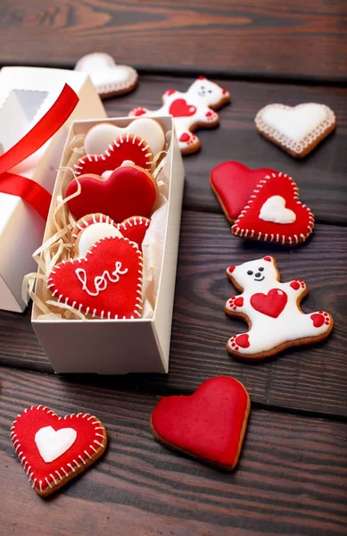 Red cookies hearts, white bears with red icing and white box with ribbon bow on the brown wooden table.Gift for Valentine\'s Day.Valentine day background.Top view