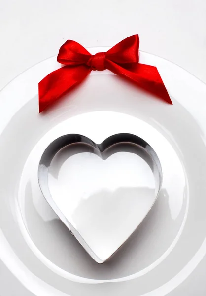 Metal heart mold on white plate with red ribbon bow.Background for valentine 's day.Minimalism.Copy space.Closeup — стоковое фото