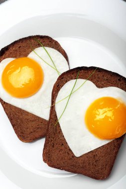 İki tost ile pişmiş yumurta beyaz bir plaka üzerinde bir kalp şeklinde. Taş koyu arka plan üzerinde. Yazıt kırmızı saten kurdele sevgisi. Yaratıcı Sevgililer günü arka plan. Aşk concept.closeup.Breakfast