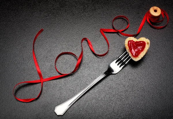 Inscripción, palabra amor de cinta de satén rojo y corazón de pan tostado con mermelada roja en fork.Valentine fondo del día. Concepto de amor. En fondo de piedra oscura. Creative.Love fondo —  Fotos de Stock