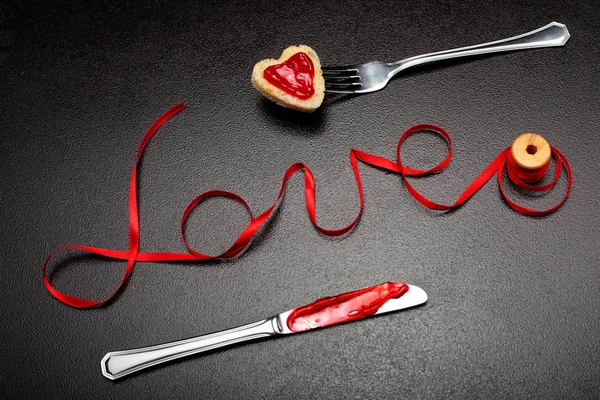 Inscription, word love of red satin ribbon and heart of toast bread with red jam on fork and knife with jam.Valentine day background.Love concept.On dark stone background.Creative.Love background