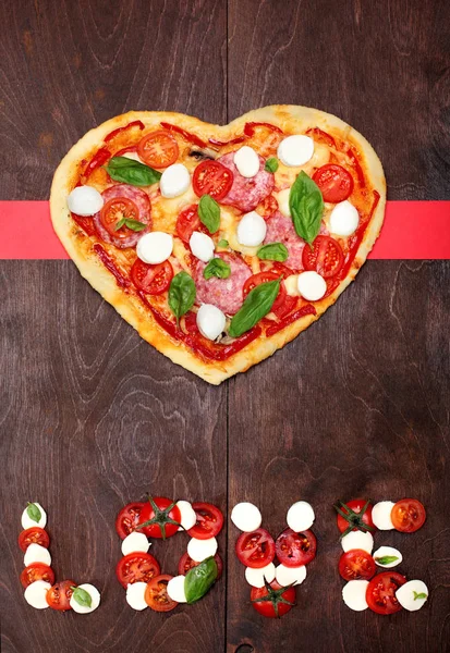 Restaurace Pizza ve tvaru srdce s salámem, rajčaty, bazalkou a mozzarelou tmavé dřevěné hnědé pozadí. Nápis love rajčata mozzarellou a bazalkou. Pohled shora. Creative valentine den pozadí. — Stock fotografie