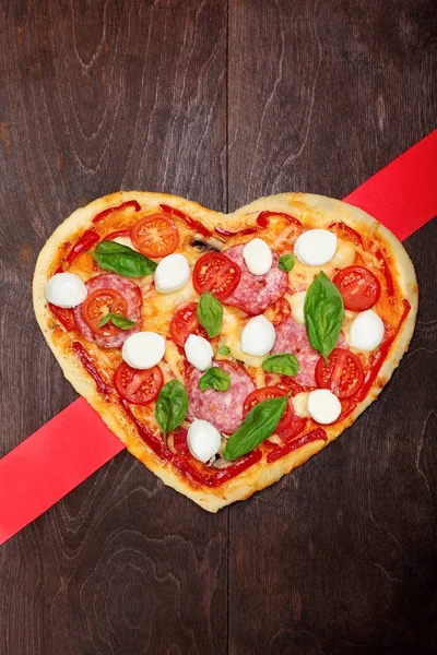 Restaurace Pizza ve tvaru srdce s salámem, rajčaty, bazalkou a mozzarelou tmavé dřevěné hnědé pozadí. Kopírovat prostoru. Pohled shora. Creative valentine den pozadí. Láska koncept — Stock fotografie