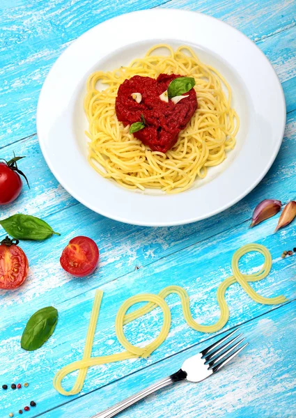 Spaghetti, Pasta.Toamtoes sauce i shape heart.Basil, tomatoes, garlic, sea salt, pepper.Insrption love of Spaghetti.Food typography.Cyan wooden background.Valentine day.Concept love