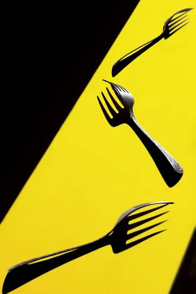 three forks parallel on a yellow background.Each casting a strong shadow.Art of shadow. Visual art