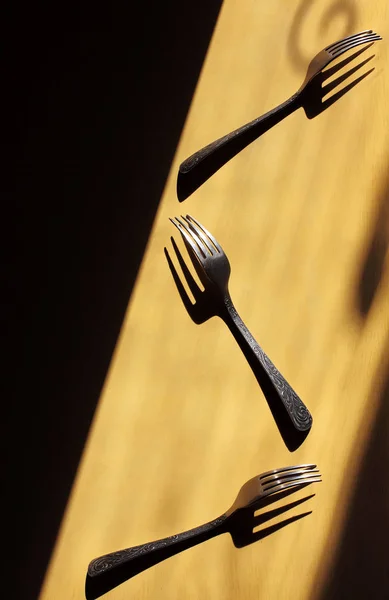 three forks parallel on a yellow background.Each casting a strong shadow.Art of shadow. Visual art