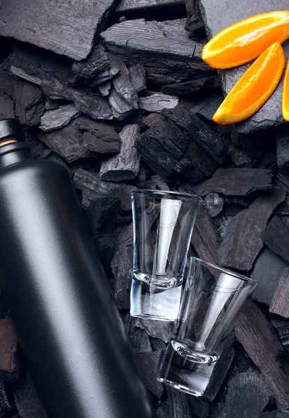 Original black matte bottle of vodka or tequila and shot glass .Slices of oranges.On charcoal background. Black edition.Creative.Let\'s drink.Cheers