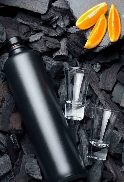 Original black matte bottle of vodka or tequila and shot glass .Slices of oranges.On charcoal background. Black edition.Creative.Let's drink.Cheers