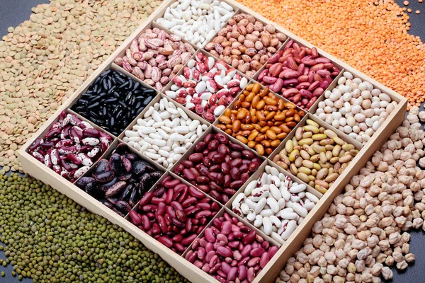 Different types of legumes beans. In wooden box.Varieties of beans.Small red bean,Scarlett runner bean Phaseolus coccineus ,butter bean,kidney bean,pinto and other sorts of beans.Top view.On dark ston