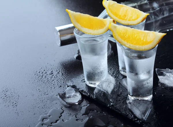 Vodka. Tomas, vasos con vodka y limón con hielo. Fondo de piedra oscura. Espacio de copia. Enfoque selectivo —  Fotos de Stock