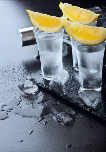 Vodka. Colpi, bicchieri con vodka e limone con ghiaccio. Sfondo in pietra scura. Copia spazio. Focus selettivo — Foto Stock