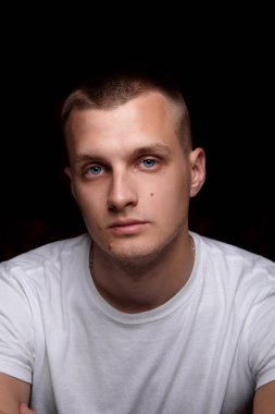 Yakışıklı beyaz delikanlı. Beyaz t-shirt. Loking ciddi. Duygu. Siyah arka plan üzerine. Portre