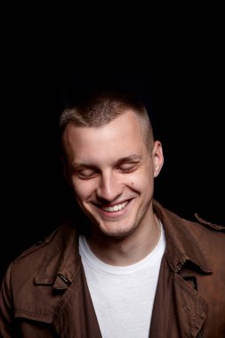 Yakın çekim yakışıklı delikanlı portresi. Tıraşsız üç gün. Hansdome adam gülüyor. koyu arka plan üzerinde. Modern ve dramatik fotoğraf. Kahverengi ceket ve Beyaz tişört. Duygu. Mavi gözlü